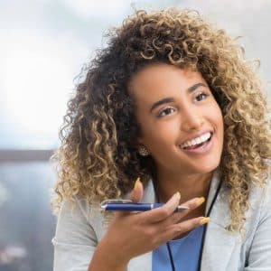 Två personer sitter och pratar. Den ena håller i en DISTANSUTBILDNING TILL INTEGRATIONSPEDAGOG-penna och ler.